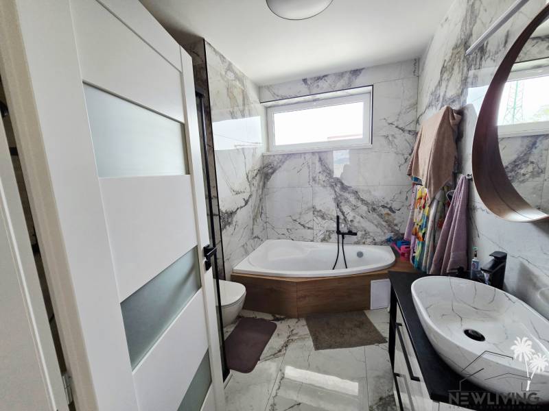 Bathroom with a mirror, bathtub, and marble tiles in a family house.