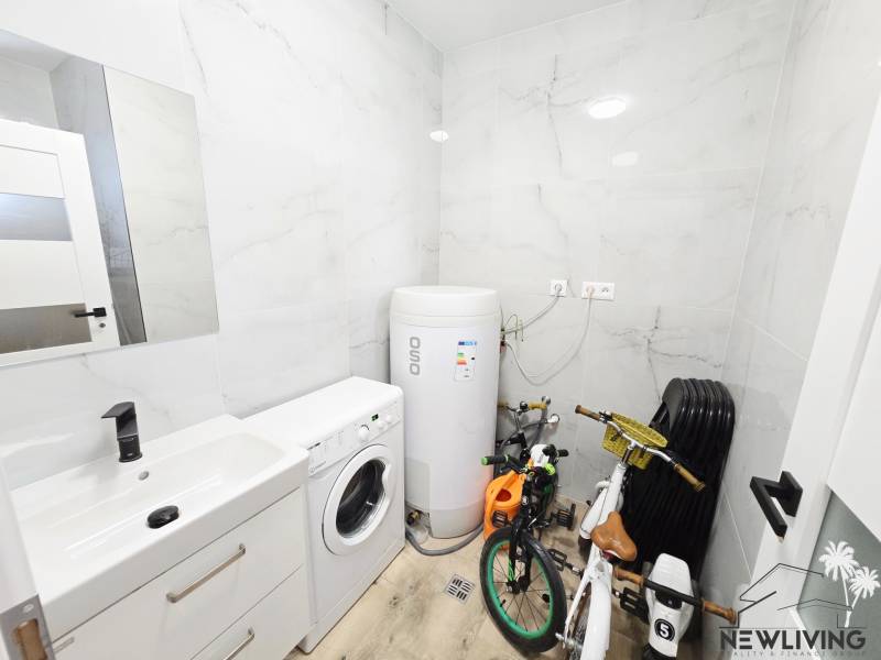 A bathroom with a sink, a washing machine, a boiler, and children's bicycles in a family house.