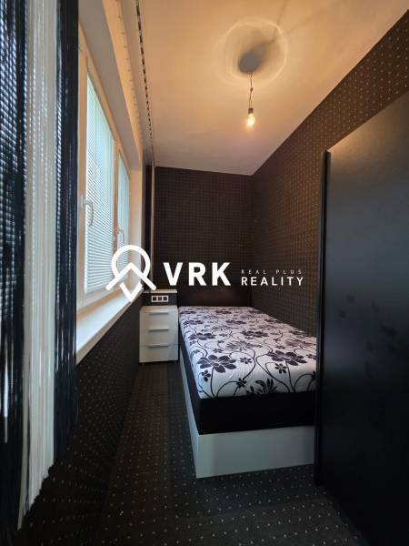 Narrow bedroom in a studio apartment with a floral mattress and black walls.