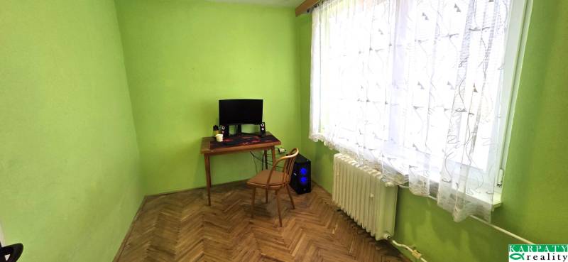 A room in a 3-room apartment with a wooden decor floor, a table, and a computer.