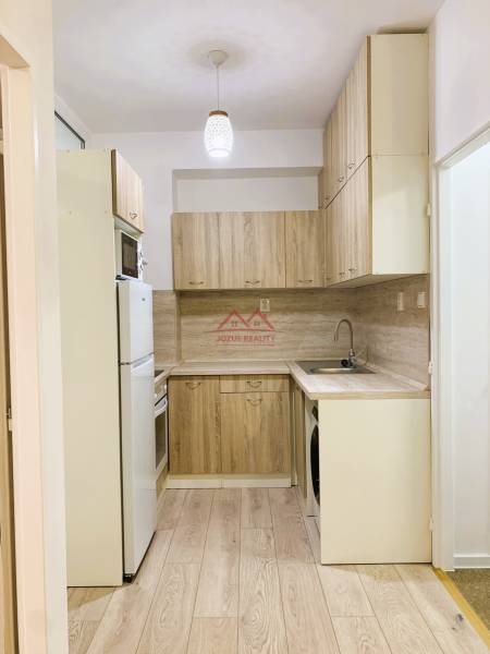 A kitchen in a 3-room apartment with wood-patterned flooring and light-colored furniture.