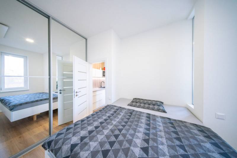 A bedroom in a 2-room apartment with a bed, a mirrored wardrobe, and a floor with a wooden decor.