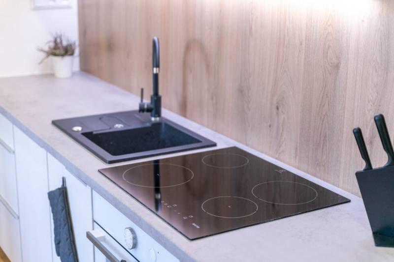 A kitchen in a 2-room apartment with an induction cooktop and a floor with a wooden decor.