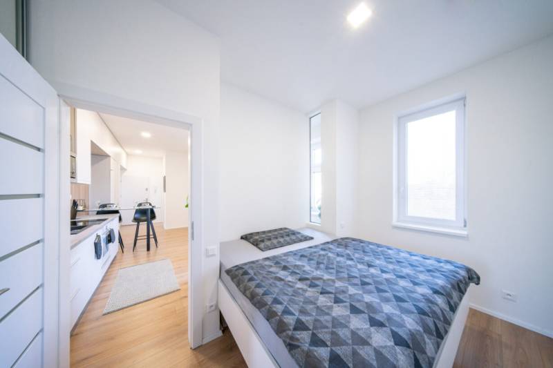 A bedroom in a two-room apartment with a wooden decor floor and a spacious bed.