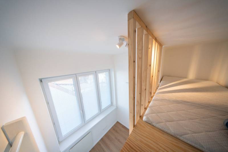 Loft bed in a 2-room apartment with a wooden-patterned floor and a large window.