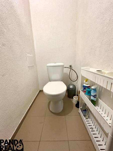 A toilet in a family house with a shelf for cleaning products and a tiled floor.