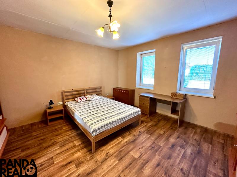 A bedroom in a family house with a bed, a table, and a floor with a wooden decor.