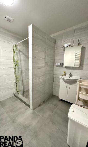 A bathroom with a shower and a sink in a family house, light tiles, gray flooring.