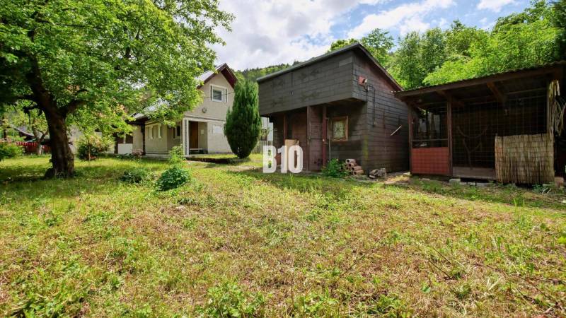 A cottage in Necpaly with a wooden shed surrounded by greenery and trees.