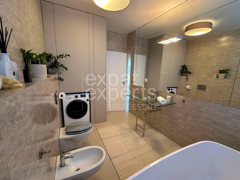 Bathroom in a 3-room apartment with a washing machine, bidet, and decorative plants. Defective mirror.