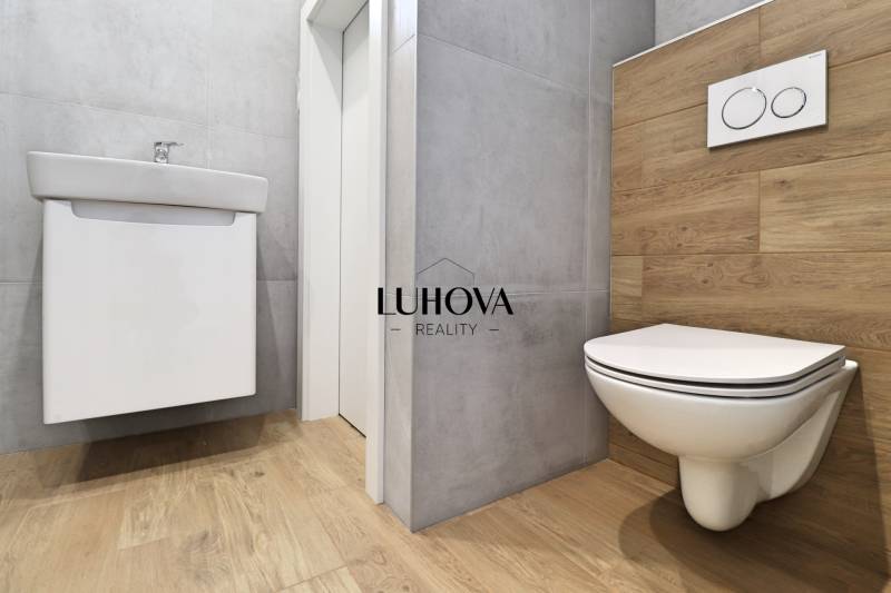 A toilet with a wooden-patterned floor and a simple sink in a family house.