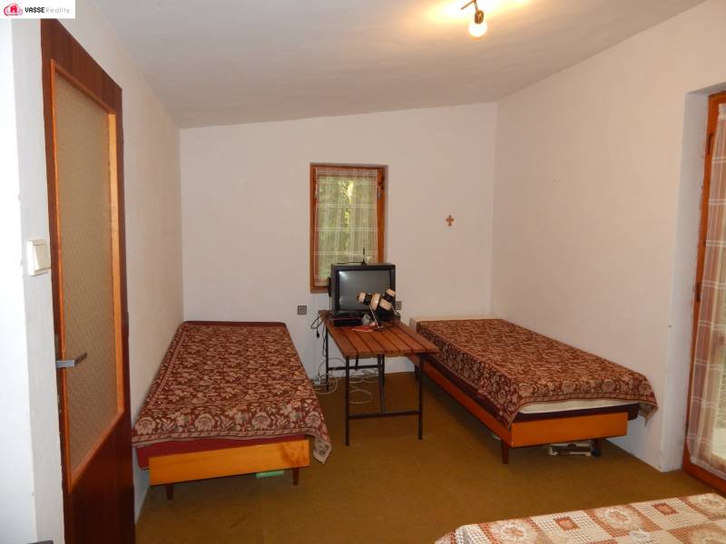 The cottage offers two beds with embroidered blankets and a small television on the table.