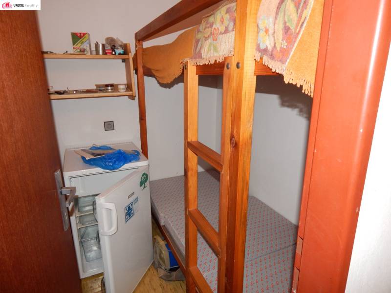 Bunk bed and small refrigerator in a room of a cabin with shelves.