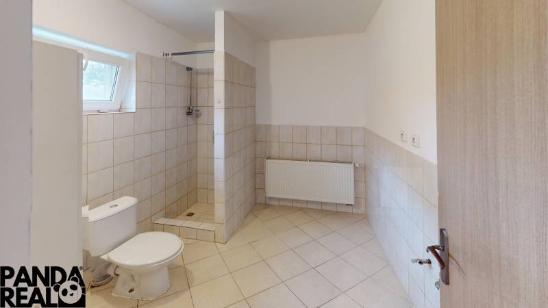 A bathroom in a family house with a toilet, shower, and window. Tiles on the walls and floor.