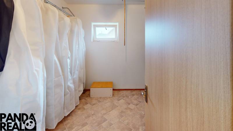 A wardrobe in a family house with clothes on hangers and a window at the top of the wall.