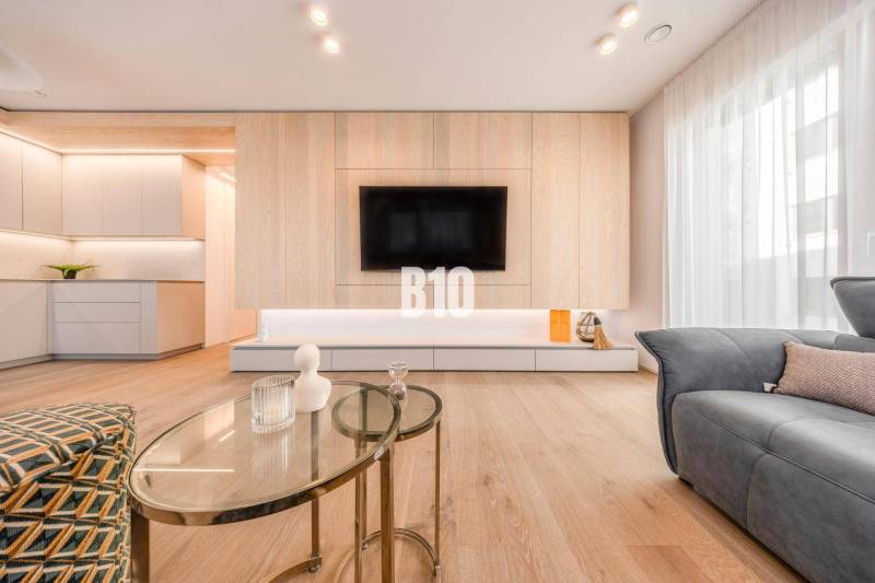 Living room in a three-room apartment with a wood-patterned floor and a TV on the wall.