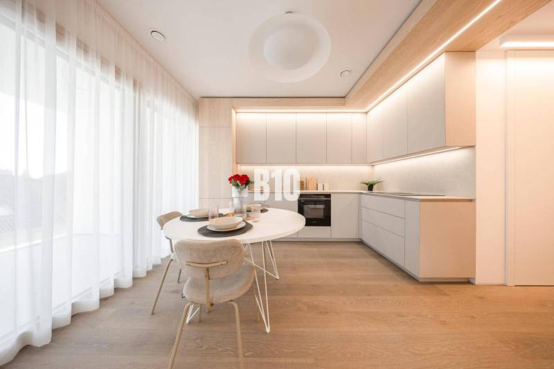 A kitchen in a 3-room apartment with white furniture and a wooden decor floor.