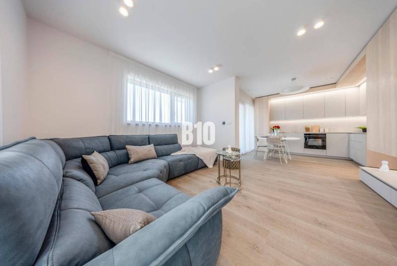 Living room with a large sofa and a kitchenette, floor with wooden decor.