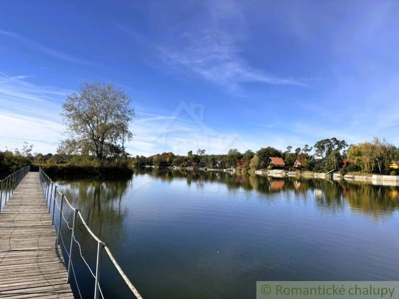 The lake near Malé Leváre with a wooden bridge and cottages in the background.