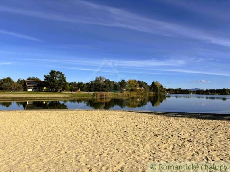 The beach by the cottage in Malé Leváre, surrounded by a lake and greenery on a sunny day.