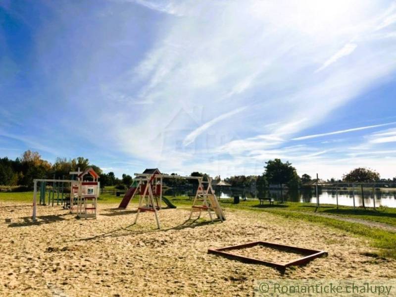 Playground by the lake in Malé Leváre with a blue sky and trees in the background.