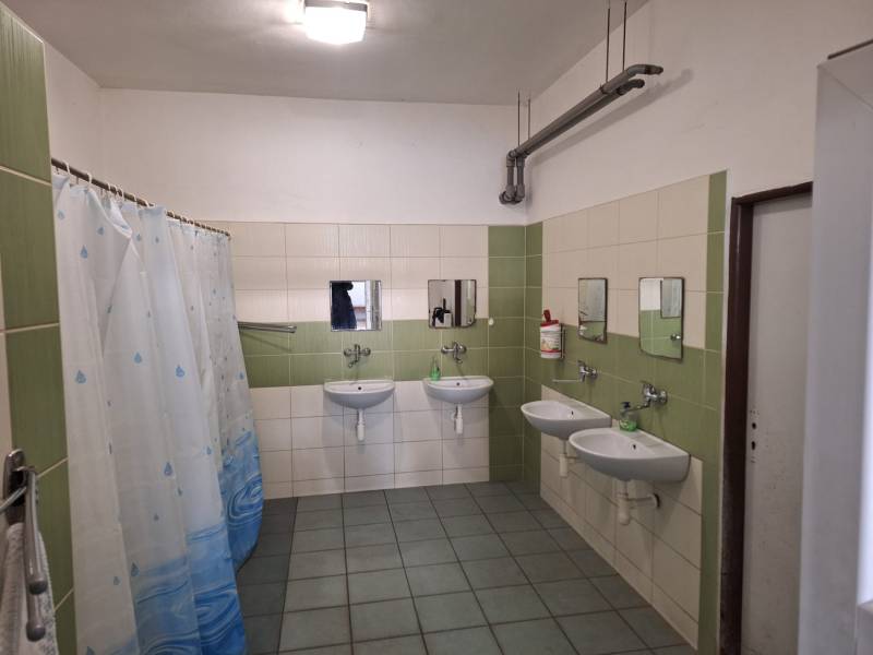 Bathroom of warehouses and halls. Three sinks, shower curtains, green and white tiles.