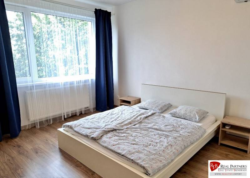 A bright bedroom with a large window, a bed, and a wooden decor floor in a 3-room apartment.