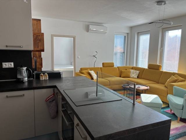 A bright living room of a three-room apartment with a yellow sofa and a kitchen island.
