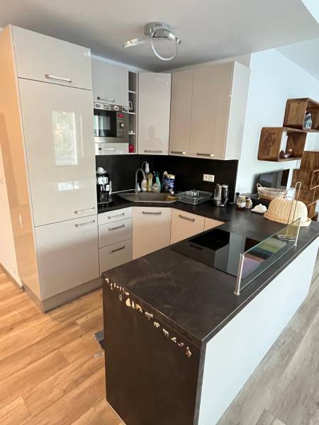 A kitchen in a two-room apartment with glossy cabinets and a floor with a wooden decor.