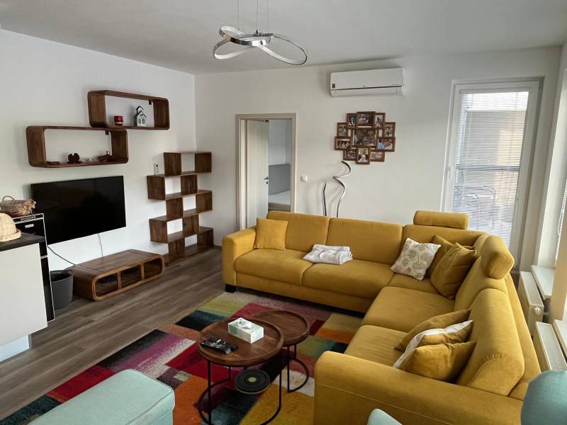 Living room in a two-room apartment with a wooden decor floor and a yellow sofa.