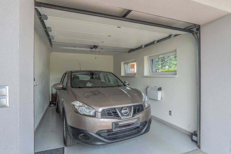A car in the garage of a family house with white walls and two windows.