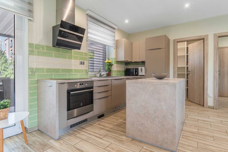A kitchen in a family house with corners, cabinets, appliances, and green tiles.