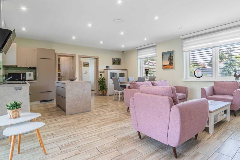 Open kitchen with living room in a family house. Light colors, pink armchairs, dining table.