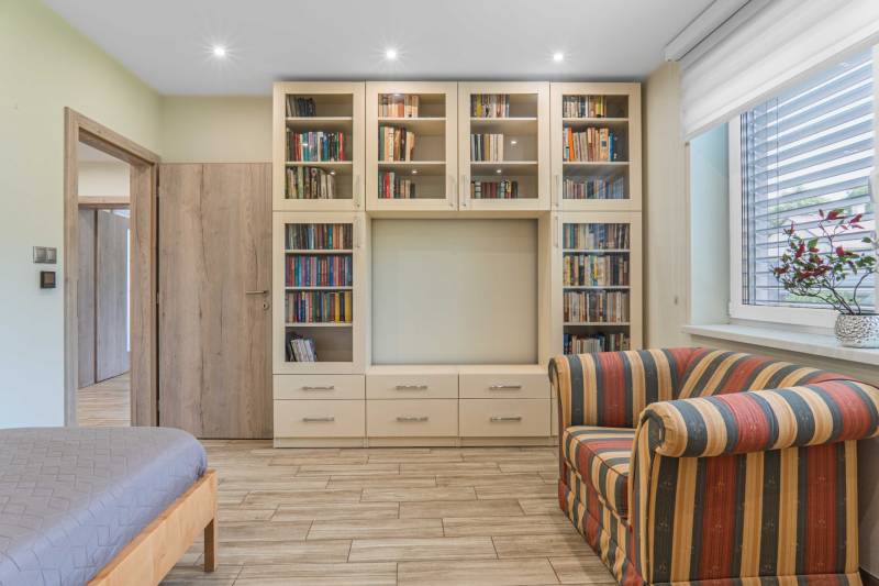 A library with books, a striped chair, and a bed in a family house.