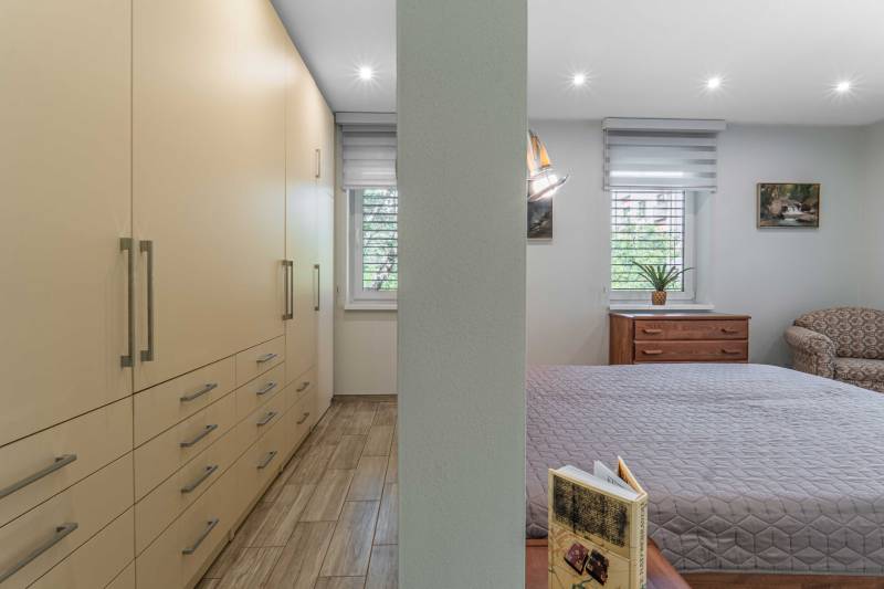 Bedroom in a family house with a bed, wardrobes, a sofa set, and windows with blinds.