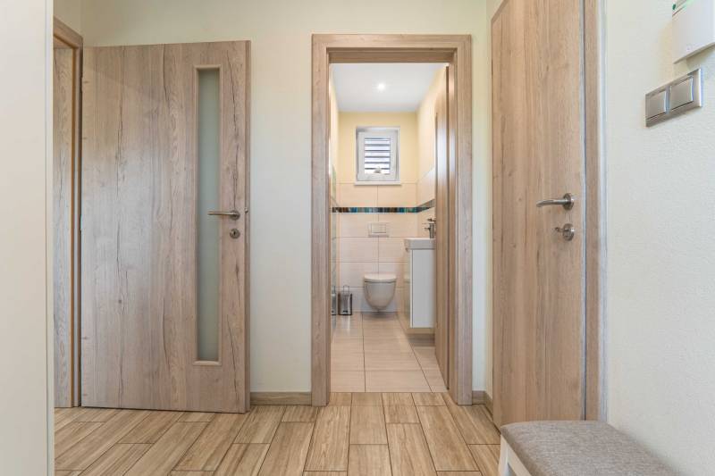 A hallway in a family house with a view into the bathroom, wooden doors, and tiles.