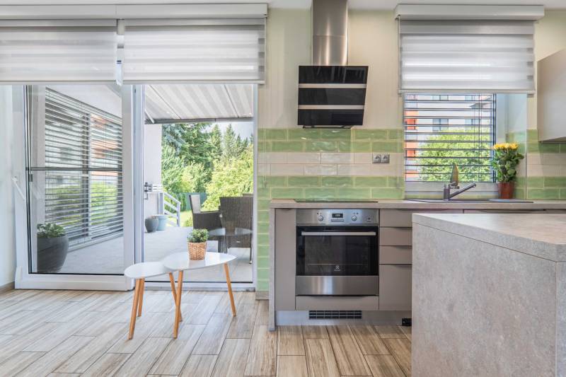 A kitchen in a family house with patio doors, green tiles, an oven, and a range hood.