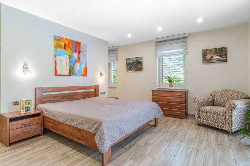 Bedroom in a family house with a bed, armchair, dresser, abstract painting, and wooden decor flooring.