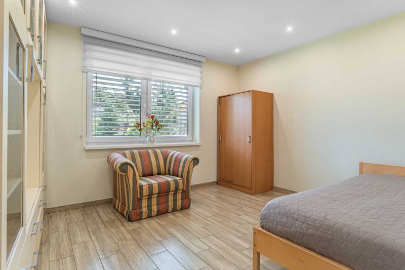 A room in a family house with an armchair, a bed, a wardrobe, and flowers on the windowsill.