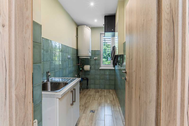 A narrow kitchen in a family house with a stainless steel sink and green tiles.