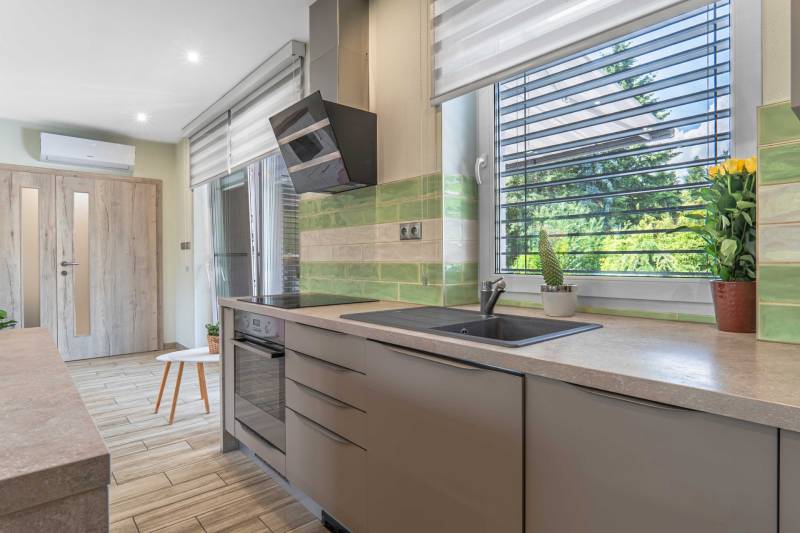 A kitchen in a family house with a modern kitchen unit, plants, and green tiles.