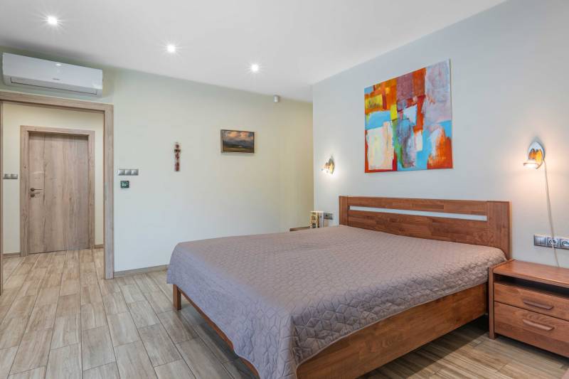 A bedroom in a family house with light walls, a wooden bed, and an abstract painting.