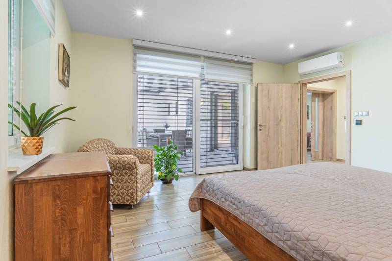 Bedroom with large doors, an armchair, a dresser, and a plant in a family house.