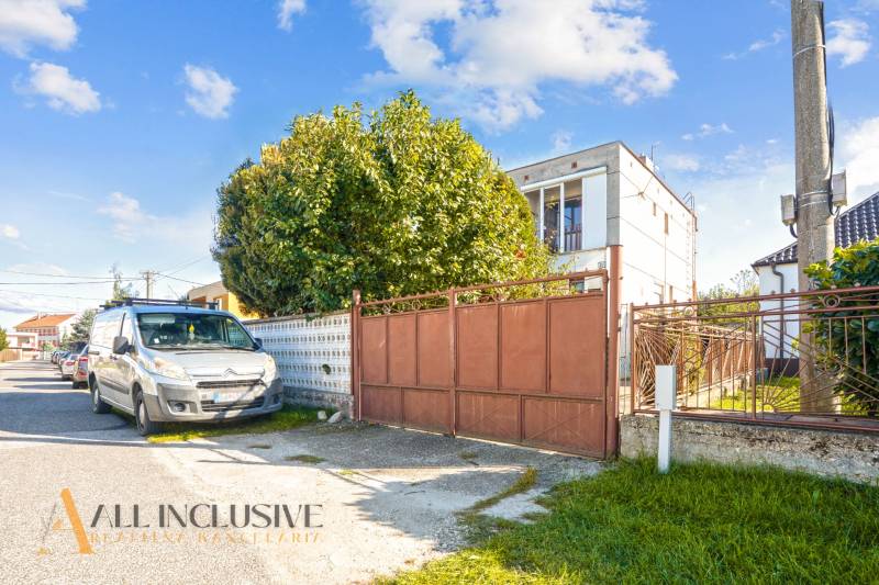 A family house in Veľká Mača with a green gate and cars parked in front of the house.
