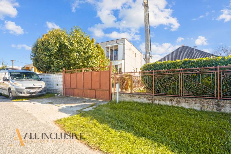 A family house in Veľká Mača with a gate, a car, and greenery in the front yard.