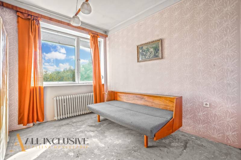 A room in a family house with orange curtains, a sofa, and a painting on the wall.