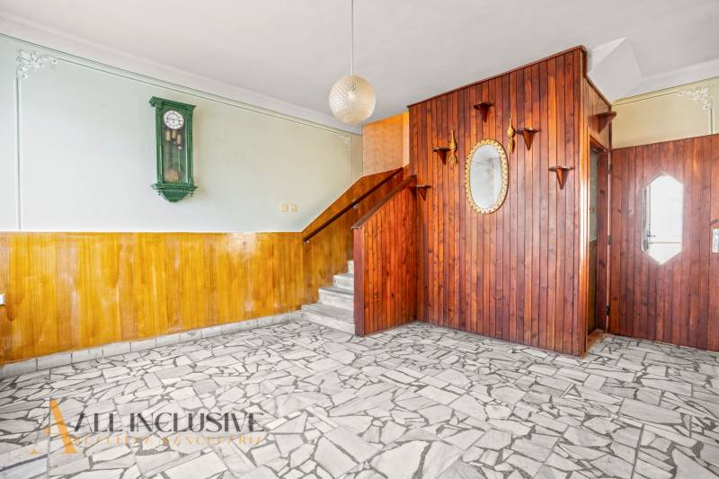 Interior of a family house with wooden paneling, wall clock, and mosaic floor.