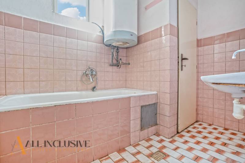 A bathroom in a family house with pink tiles and a bathtub located under the window.