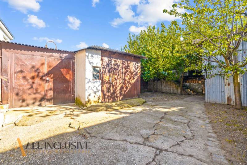 The yard at the family house in Veľká Mača with trees and a farm building.