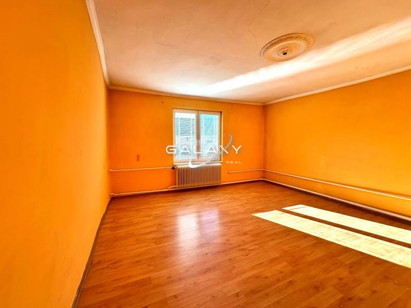 A room in a family house with orange walls and a wood-patterned floor.